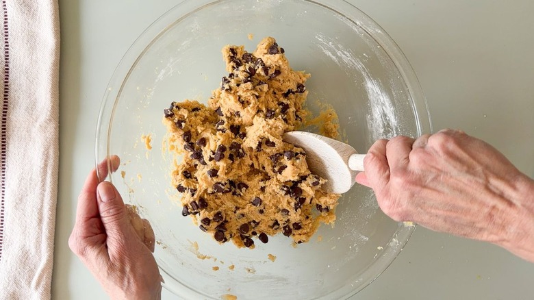 Stirring chocolate chips into cookie dough in glass bowl with wooden spoon