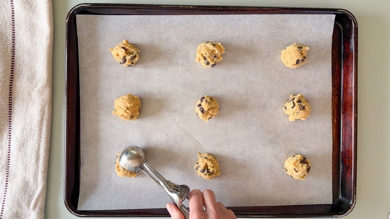Scooping chocolate chip cookie dough onto parchment-lined baking sheet