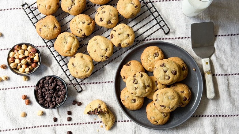 Nutella-stuffed chocolate chip cookies on cooling rack and plate with chocolate chips and hazelnuts