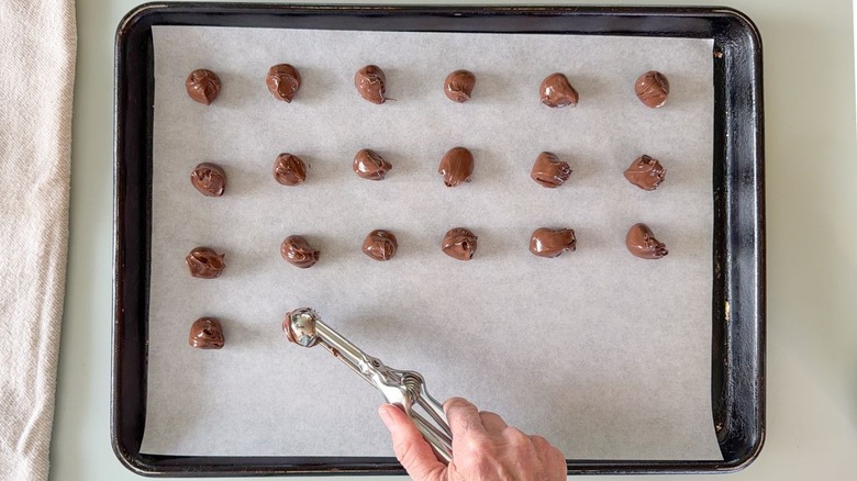 Scooping out Nutella onto parchment paper-lined baking sheet