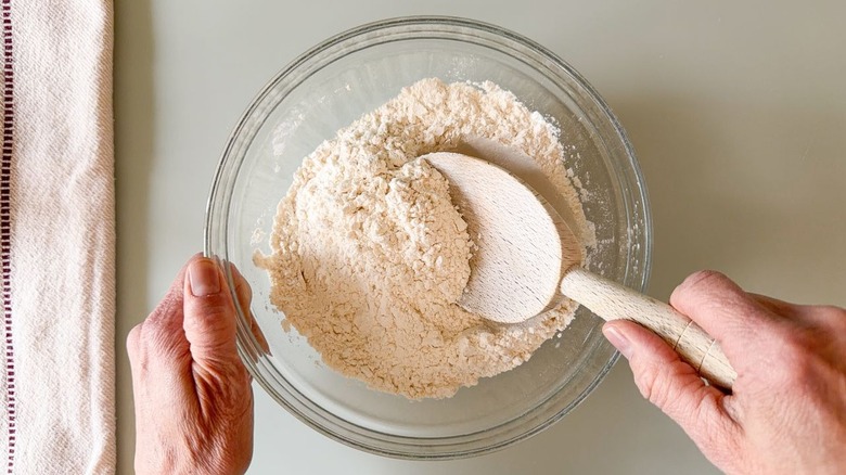 Stirring dry ingredients for chocolate chip cookies in glass bowl with wooden spoon