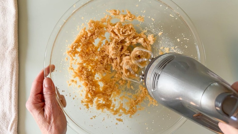Creaming together butter and brown sugar with hand mixer in glass bowl