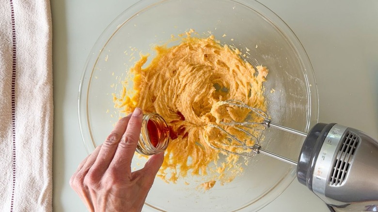 Adding vanilla to chocolate chip cookie batter in glass bowl