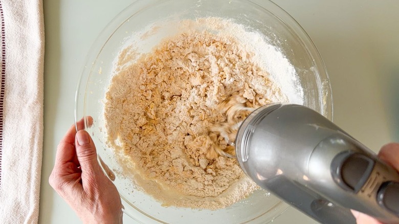 Mixing dry ingredients into cookie batter in glass bowl with hand mixer