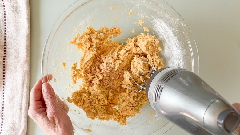 Mixing chopped hazelnuts into cookie dough in glass bowl with hand mixer