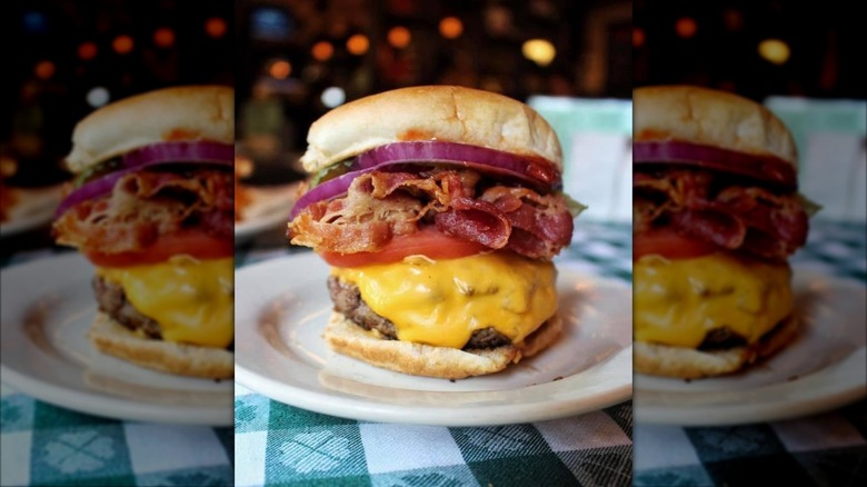 A delicious looking cheeseburger on a dark surface with various toppings and condiments on it