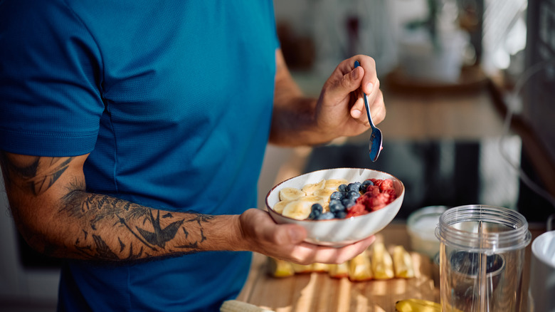 Man holding a bowl topped with bananas, blueberries, and raspberries