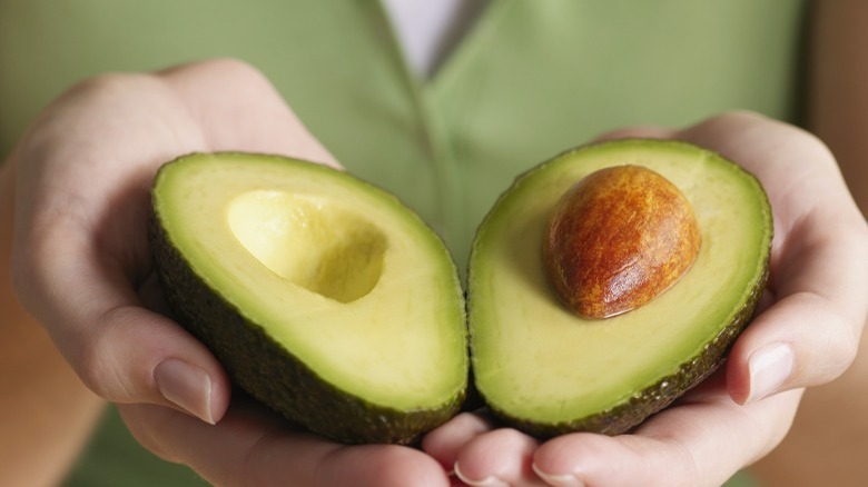 Hands holding two avocado halves