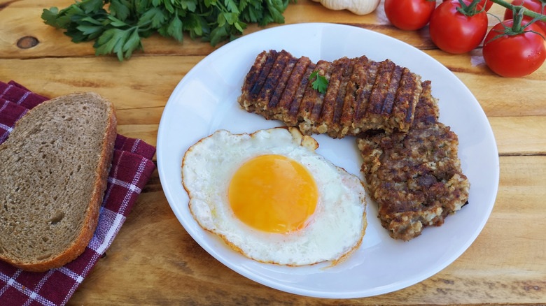 A plate of goetta with a sunny-side up egg, alongside a slice of rustic bread resting on a cloth