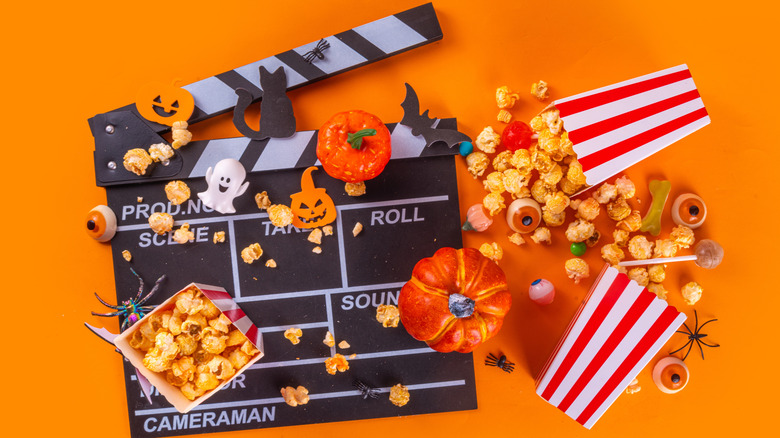 film clapper with spooky decoration and spilled popcorn on orange background