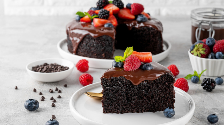 a slice of moist chocolate cake with chocolate glaze and berries on top