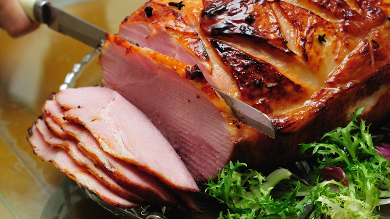A carving knife slicing a smoked ham on glass tray.