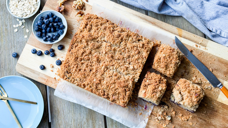Old-fashioned blueberry crumb cake on cutting board with plates, knife, and fresh blueberries