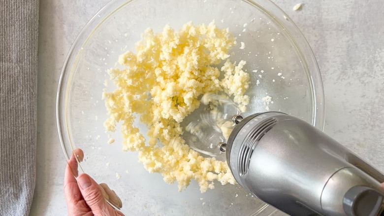 Creaming together granulated sugar and softened butter with hand mixer in glass bowl