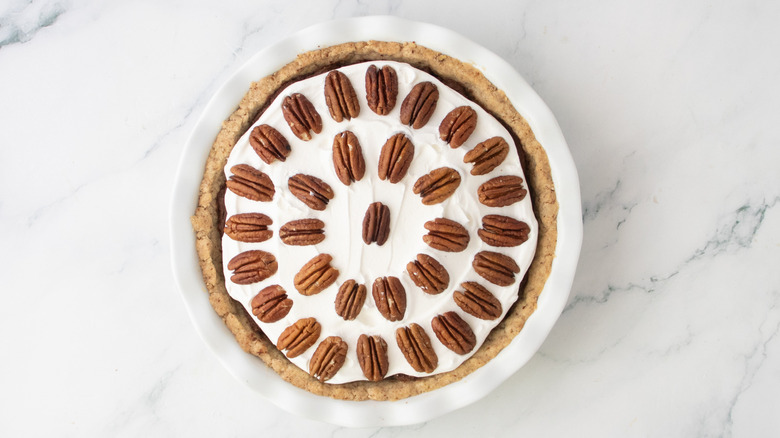 Whipped topping-topped pie garnished with pecan halves