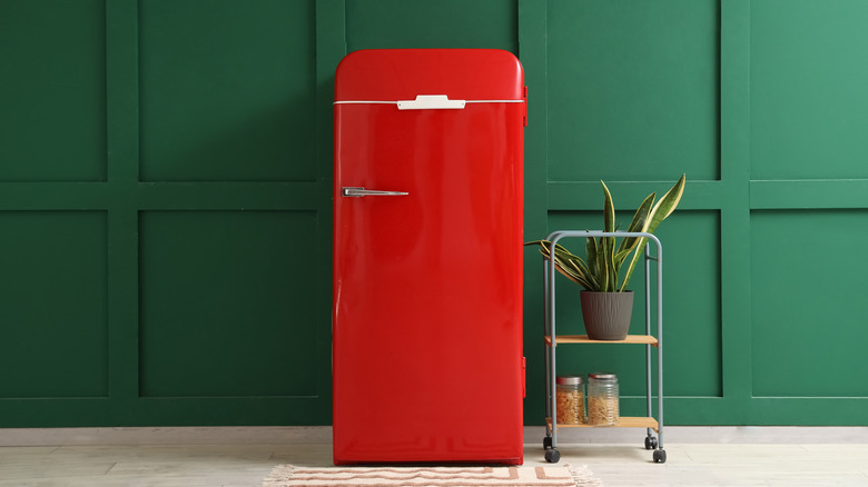 a red vintage-style refrigerator against a green wall with a cart on the side