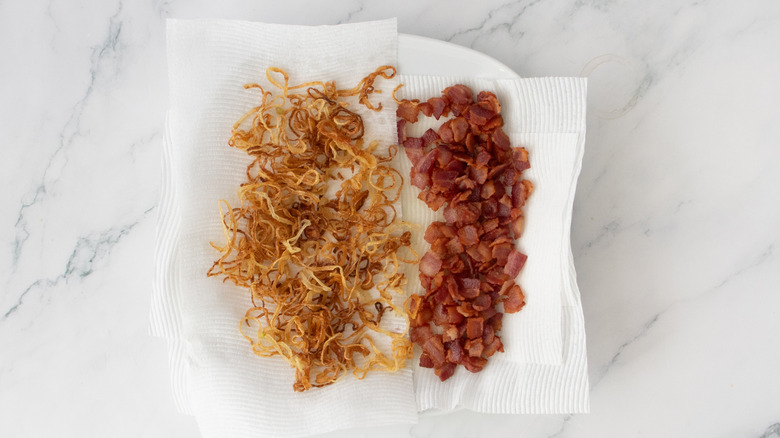Fried onions and cooked bacon on a plate with paper towels