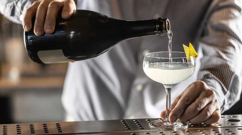 A bartender pouring champagne into a French 75 cocktail