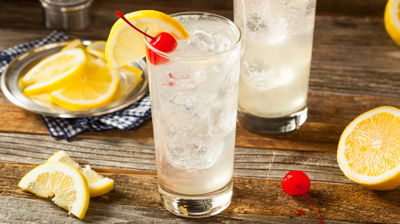 A Tom Collins cocktail garnished with a slice of lemon and a cherry