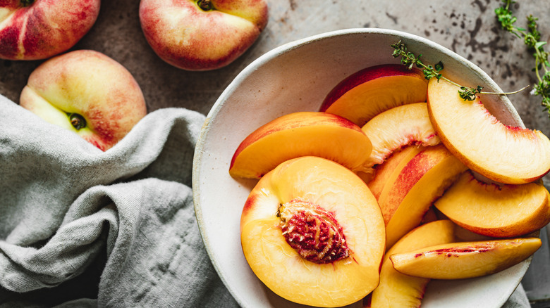 A lovely bowl of halved and sliced peaches beside whole fruits.