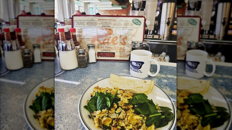 A plate of scrambled eggs on the counter next to a Rae's mug and menu