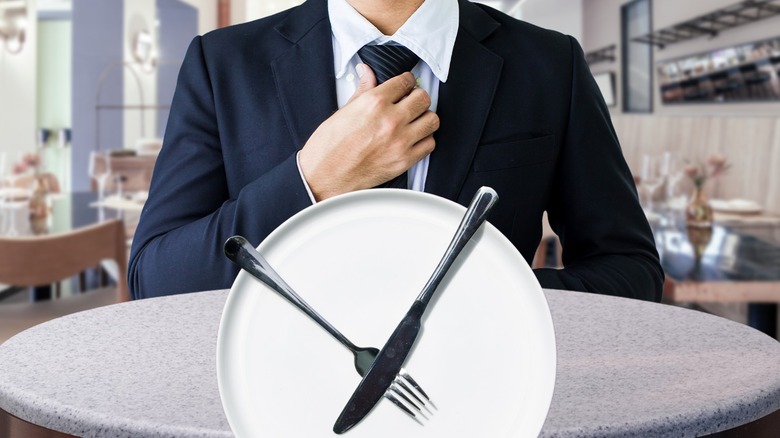 Waiter straightening his tie and a white plate with a fork and knife laid across it