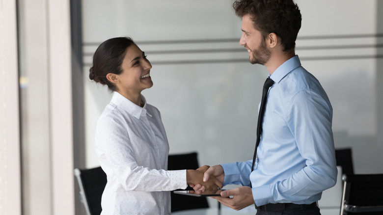 Man standing greeting a woman and shake her hand