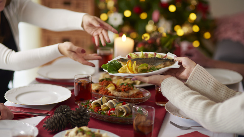 People passing a serving plate at a dinner table during the holidays
