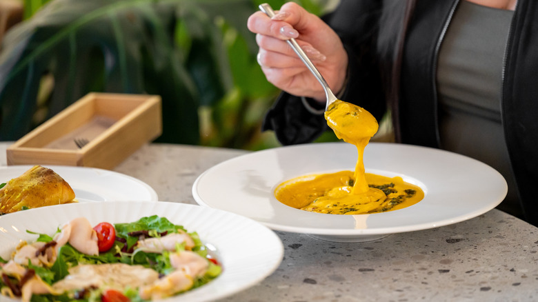 Person eating soup from a white bowl with a spoon