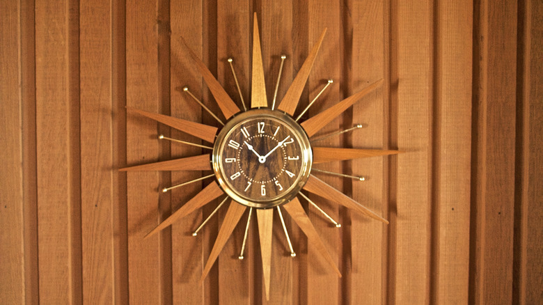 A vintage sunburst clock on a wood panel wall