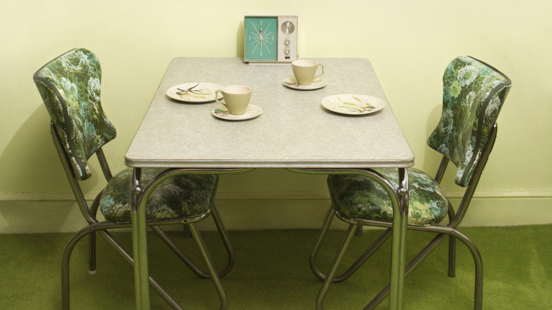 Two green chairs at a formica table with teacups and a clock