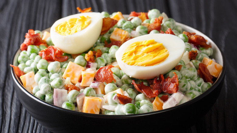 A bowl of pea salad topped with hard-boiled eggs on a wooden table.