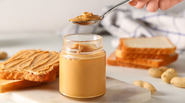 glass jar full of peanut butter surrounded by peanuts