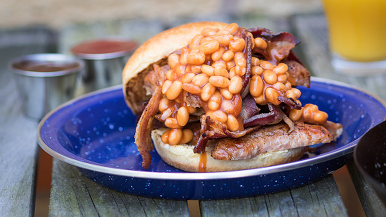 Baked beans, bacon, and meat piled high on a brioche bun on a blue plate