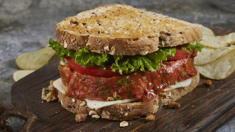 Turkey meatloaf slice on toasted multigrain bread with lettuce and tomato, on a wood board surrounded by potato chips