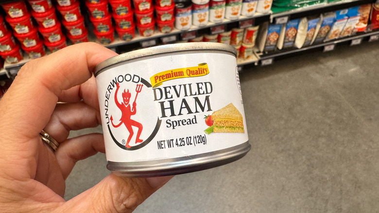 A hand holds a can of Underwood deviled ham spread at a grocery store