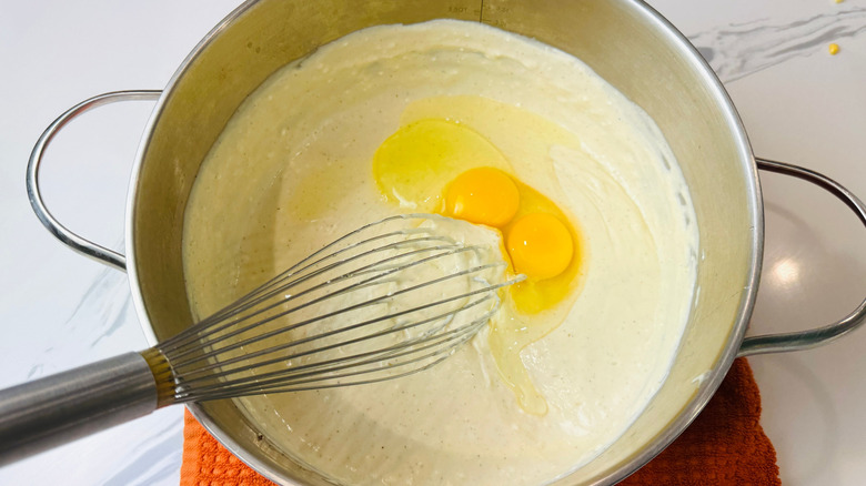 Whisking eggs into cheese sauce in pot
