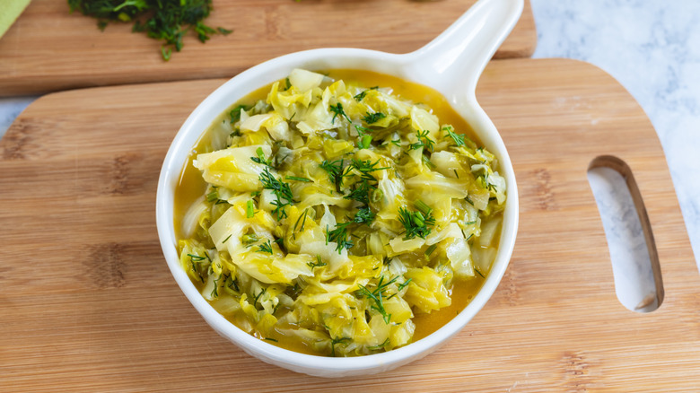 Stewed young cabbage with butter and dill on a wooden chopping board