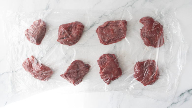 Eight filet mignon steaks between sheets of plastic wrap
