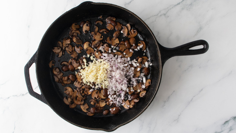 Sauteed mushrooms in a skillet topped with minced shallot and garlic