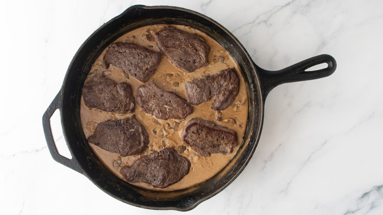Seared steaks in a large skillet with brown mushroom sauce