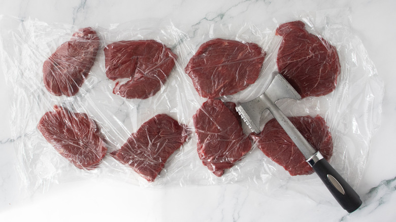 Filet mignon steaks between sheets of plastic wrap with meat mallet
