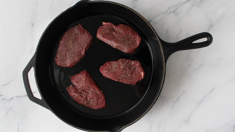 Four raw filet steaks in large skillet