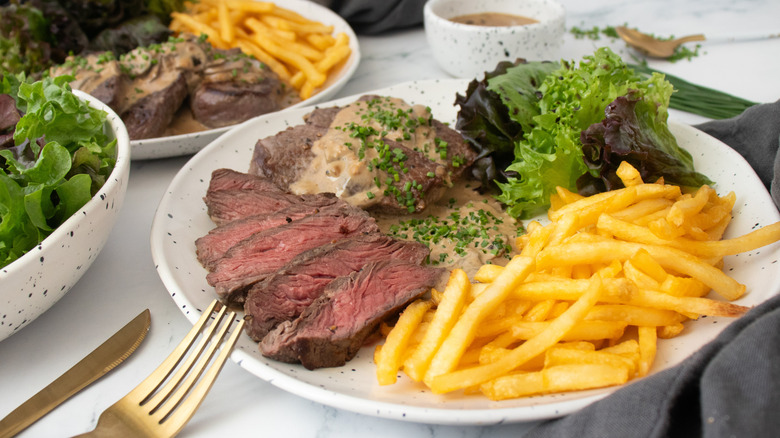 Side shot of Steak Diane with frites and salad