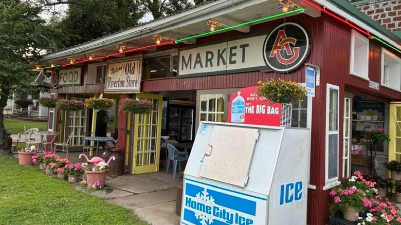 Exterior of the Old Riverton Store with blooming flowers and an ice machine