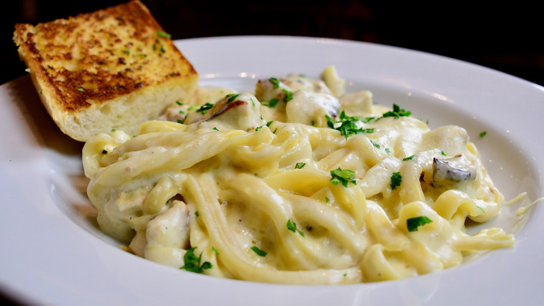 Alfredo sauce on pasta in a bowl with a side of garlic bread toast.