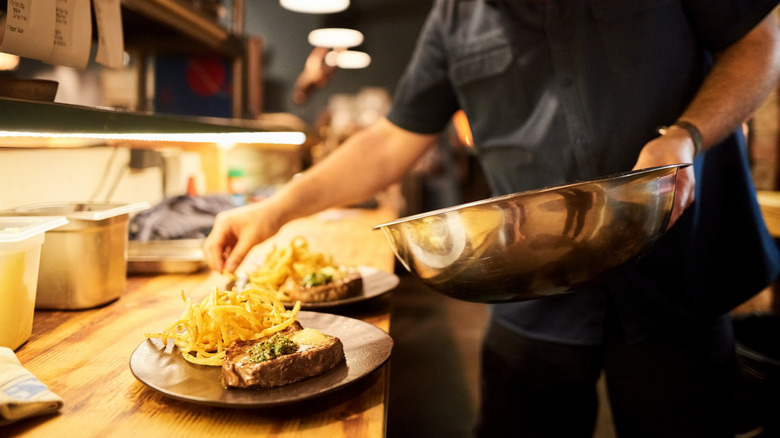 A person in the kitchen adjusting the plating of a dish