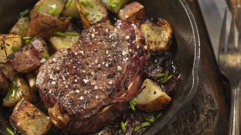 A crispy steak topped with coarse atop a pile of roasted potatoes