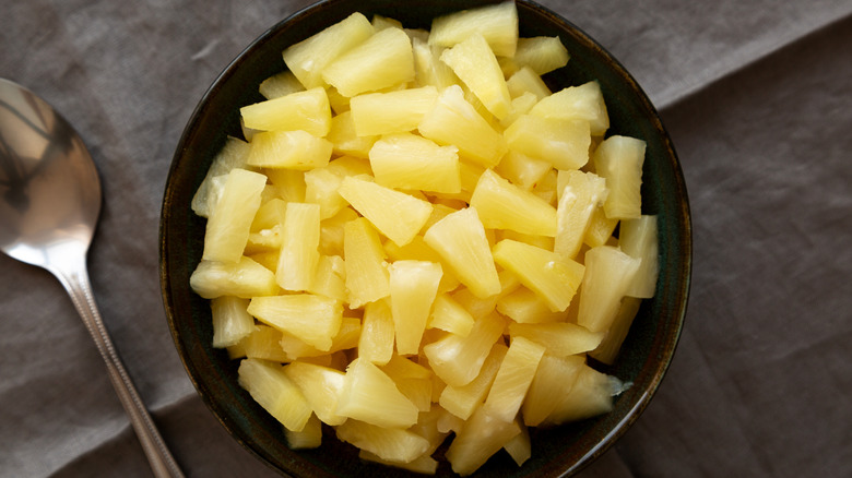 A black bowl of pineapple tidbits is photographed from overhead.