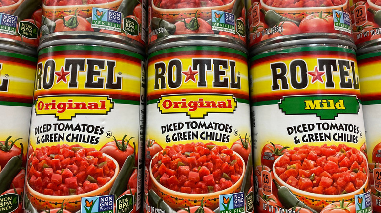 Cans of Rotel are stacked on a grocery store shelf